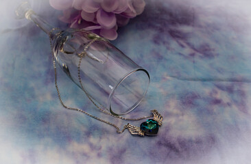 Champagne glass with a beautiful blue gem heart necklace on a blue and purple background, with flowers in the back. 