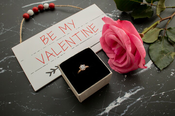 Romantic proposal surprise. Diamond ring with a single pink rose and a wooden Valentine sign, 