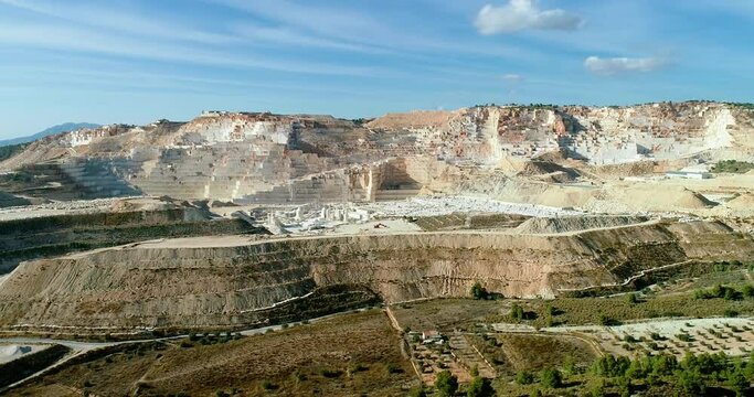 Panoramic view over a white quarry in Spain with industrial extraction. There is mountains all over the horizon under the blue sky 4K