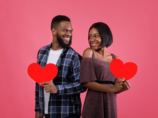 Pair of sweethearts with red hearts looking at each other with love, celebrating Valentine's Day on pink background