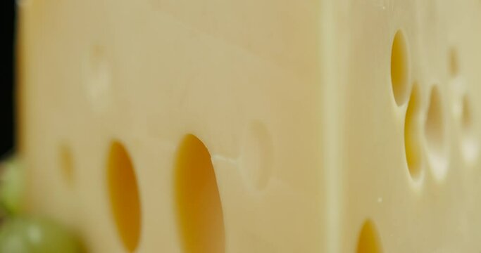 Close up part of Medium hard cheese head edam gouda parmesan on wooden board, with nuts and grapes rotaiting on the plate.