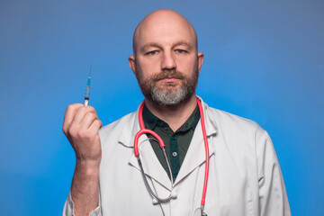 Bald medic in white uniform holding a syringe in his hand. Model in his 40s with beard. Vaccination...