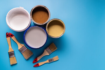 Cans with paint of different colors and painbrushes on blue background.