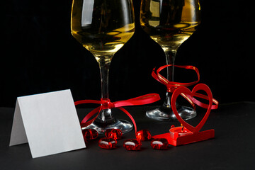 Glasses with champagne tied with a red ribbon on a black background greeting card and a candlestick in the shape of a heart