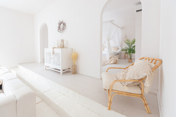 Cozy interior of a bright Balinese-style apartment with white walls, bamboo chair, big white sofa and decorations