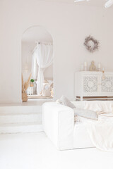 Cozy interior of a bright Balinese-style apartment with white walls, bamboo chair, big white sofa and decorations