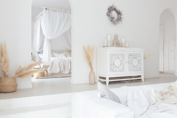 Cozy interior of a bright Balinese-style apartment with white walls, bamboo chair, big white sofa and decorations
