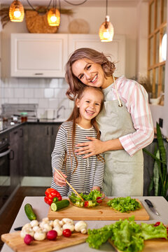 family mother with daughter cooking together, happy girl is glad to help mother preparing salad, carving fresh vegetables