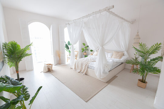 Cozy interior of a bright Balinese-style apartment with white walls, bamboo furniture. bed room with night lights, bed with balanchin and large windows