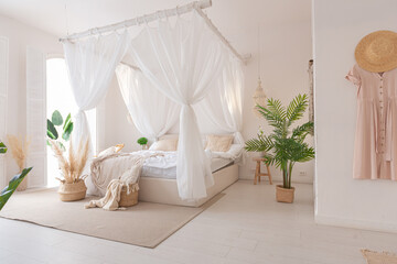 Cozy interior of a bright Balinese-style apartment with white walls, bamboo furniture. bed room with night lights, bed with balanchin and large windows