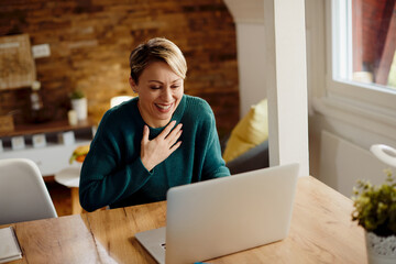 Happy woman laughing while having video call over laptop at home. - obrazy, fototapety, plakaty
