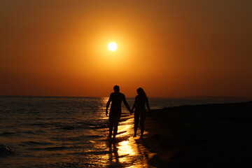 Silhouette Young romantic couple walks along the coast at sunset and hold hands