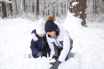 Fototapeta na wymiar Mom and daughter play snow games, build a fortress, make snowballs. Winter entertainment outside, active recreation, fun in the cold in warm clothes. Outdoor recreation, fun childhood, strong family