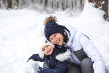 Fototapeta na wymiar Mom and daughter play snow games, build a fortress, make snowballs. Winter entertainment outside, active recreation, fun in the cold in warm clothes. Outdoor recreation, fun childhood, strong family