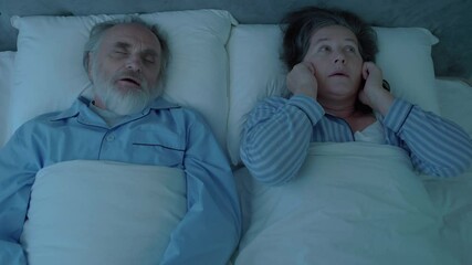 Irritated woman covering ears, listening to snoring husband, sleepless night