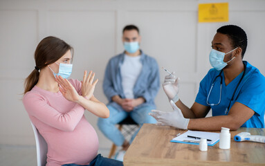 Pregnant woman in face mask scared to make coronavirus vaccine injection, making STOP gesture at clinic, panorama