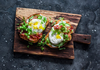Sandwiches with bacon, cream cheese, poached egg and green salad on a wooden cutting board on a...