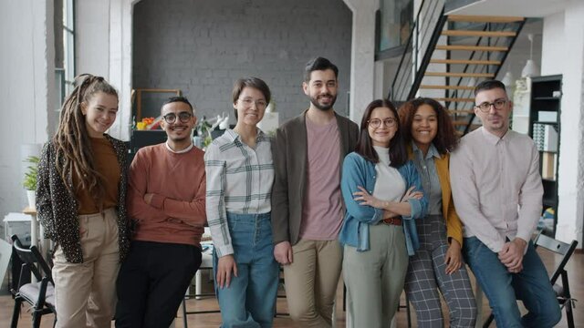 Portrait of attractive young people men and women standing in shared office smiling and looking at camera with happy faces. Multiracial team and youth concept.