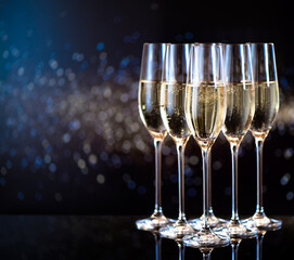 glasses of champagne for a toast in a celebratory atmosphere on mirrored bar counter in front of golden flakes  bokeh background 