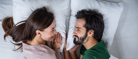 Top view of young couple in love lying on bed indoors at home.