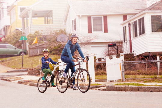 Family bike portrait with little happy boy ride on a tow tandem bicycle attached to father on urban street side view