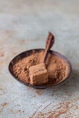 Dark chocolate truffle sprinkled with cocoa powder and cocoa powder in wooden bowl, light concrete background.