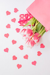 Flat lay composition with pink tulips and gift box in paper bag on white background