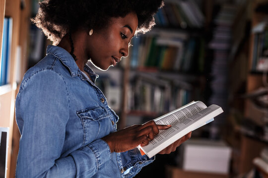 Young black female student reading a book in college library.	
