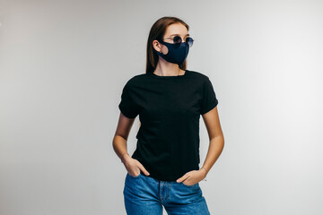 Stylish girl in glasses and protective mask wearing black t-shirt posing in studio