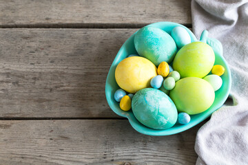 Obraz na płótnie Canvas colorful easter eggs in a turquoise plate on a shabby wooden background