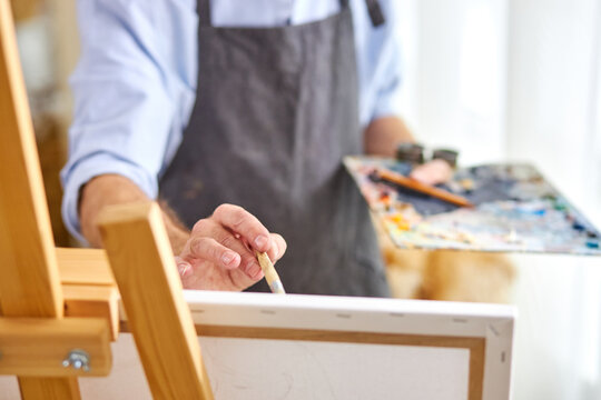 artist applying paint on canvas with paintbrush, his mind full of imagination, creative painter during work. close-up, focus on hands