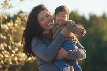 Chinese mother holding young daughter smiling at camera.
