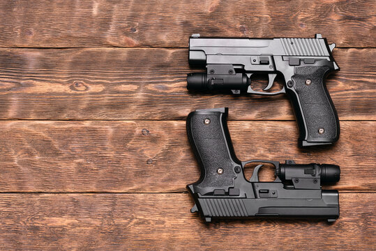 Two toy guns with laser sights on the brown wooden table background with copy space.