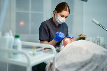 Beautician is making cure procedure on patient's face.Doctor drops medicine on woman forehead from a syringe.