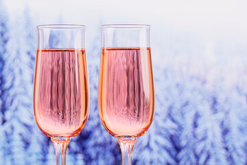 Two glasses of rose champagne with winter snowy forest bokeh as a background. Romantic dinner. Winter, Christmas or New Year holiday concept.