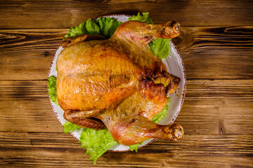 Plate with roasted whole chicken and lettuce leaves on a wooden table. Top view
