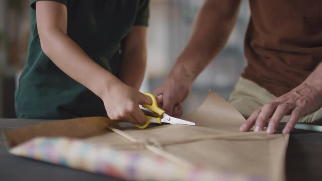 Midsection footage of unrecognizable little boy hands cutting craft paper while making diy flying kite together with father at home