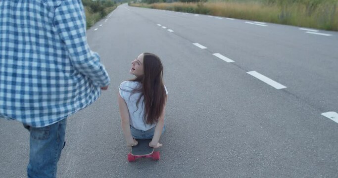 Couple of teenagers having fun time on road out of city. during skateboarding