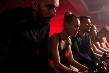 fit people riding stationary bikes together during a cardio workout session at the gym, concentrated on workout looking forward