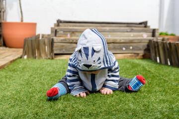 Simpática bebé jugando sentada en el jardin de casa con sudadera