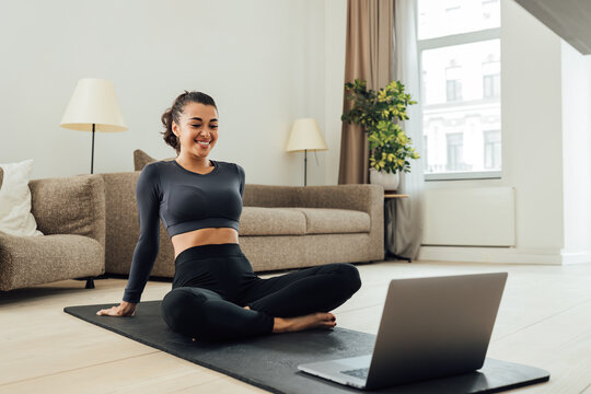 Smiling woman in sportswear sitting on a mat in the living room looking at laptop