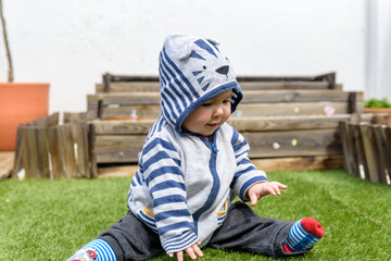 Simpática bebé jugando sentada en el jardin de casa con sudadera