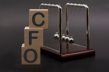 text CFO Chief Financial Officer on vertical row of wooden blocks and Newton's cradle