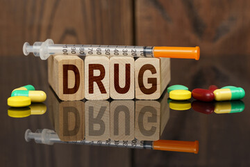 On the surface are visible tablets, a syringe, wooden dies and their reflections on which it is written - DRUG