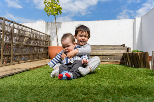 Simpática pareja de hermanos chico y chica jugando sentados juntos en el jardin de casa