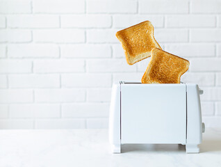 Roasted toast bread popping up of toaster with white brickwall