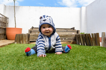 Simpática bebé jugando sentada en el cesped en jardin de casa con sudadera con capucha