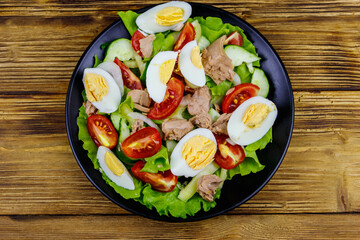 Tasty tuna salad with eggs, lettuce and fresh vegetables on wooden table. Top view