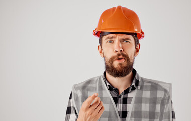 the architect gestures with his hands in an orange hard hat on a light background and a reflective vest