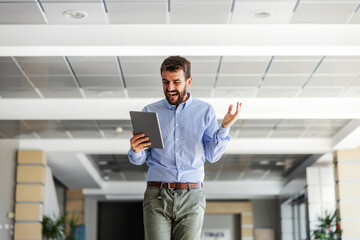 Fototapeta premium Smiling bearded excited businessman walking trough his firm and looking at tablet. He received good news.